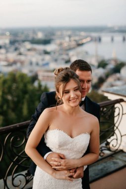 Şehrin ve nehrin zeminine karşı yüksek bir binanın çatısında genç bir çift gelin ve damat