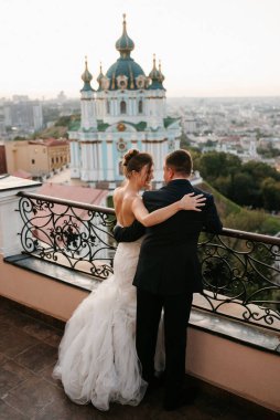 Şehrin ve nehrin zeminine karşı yüksek bir binanın çatısında genç bir çift gelin ve damat