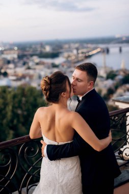 Şehrin ve nehrin zeminine karşı yüksek bir binanın çatısında genç bir çift gelin ve damat