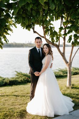 Gelin ve damat gün batımında parkta yürüyor.