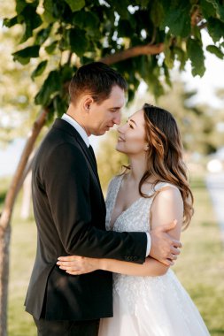 Gelin ve damat gün batımında parkta yürüyor.