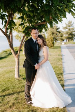 Gelin ve damat gün batımında parkta yürüyor.