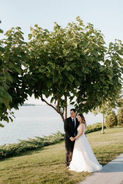 Gelin ve damat gün batımında parkta yürüyor.