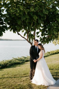 Gelin ve damat gün batımında parkta yürüyor.