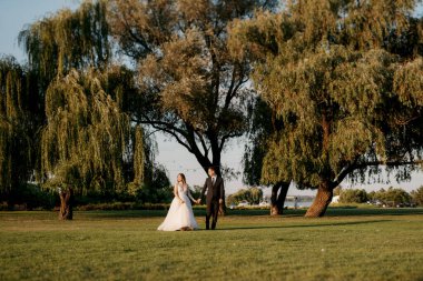 Gelin ve damat gün batımında parkta yürüyor.