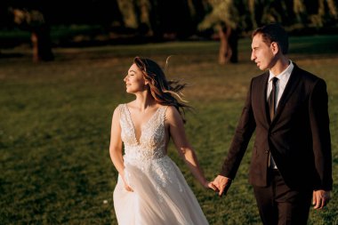 Gelin ve damat gün batımında parkta yürüyor.