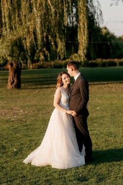 Gelin ve damat gün batımında parkta yürüyor.