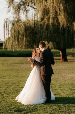 Gelin ve damat gün batımında parkta yürüyor.