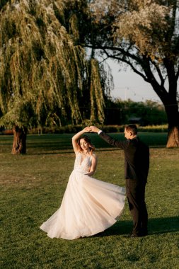 Gelin ve damat gün batımında parkta yürüyor.