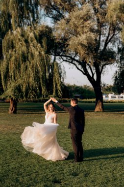 Gelin ve damat gün batımında parkta yürüyor.