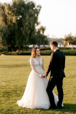 Gelin ve damat gün batımında parkta yürüyor.