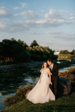 Gelin ve damat gün batımında parkta yürüyor.