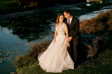 Gelin ve damat gün batımında parkta yürüyor.