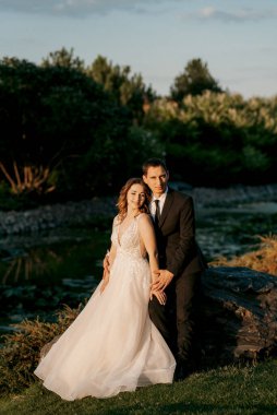 Gelin ve damat gün batımında parkta yürüyor.