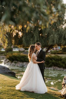 Gelin ve damat gün batımında parkta yürüyor.