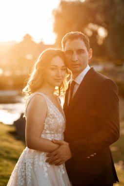 Gelin ve damat gün batımında parkta yürüyor.