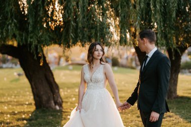 Gelin ve damat gün batımında parkta yürüyor.