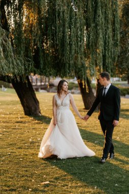 Gelin ve damat gün batımında parkta yürüyor.