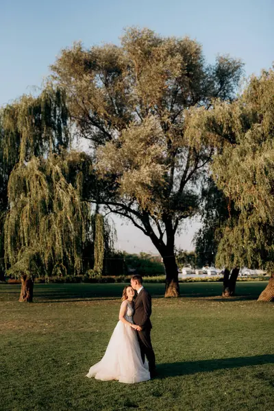 Gelin ve damat gün batımında parkta yürüyor.