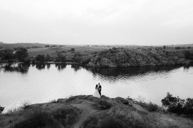 Genç bir çift, bir adam ve bir kız nehir kenarındaki yeşil tepeler boyunca yürüyorlar.