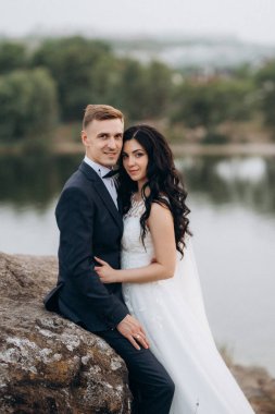 Genç bir çift, bir adam ve bir kız nehir kenarındaki yeşil tepeler boyunca yürüyorlar.