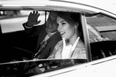 Gelin ve damat cam bir gökdelenin yanında siyah bir arabayla