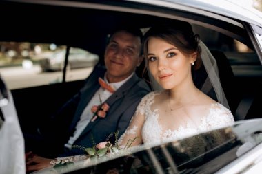 Gelin ve damat cam bir gökdelenin yanında siyah bir arabayla