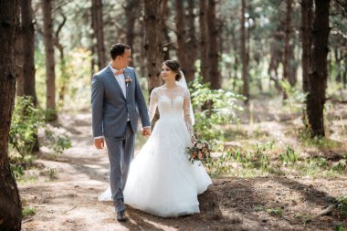 portrait of an elegant groom in a blue suit in a deciduous forest with a bouquet