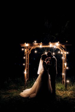 Gelin ve damat, sıcak bir ateş eşliğinde bir akşam düğün kemerine karşı.