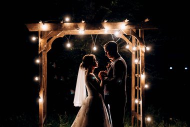 Gelin ve damat, sıcak bir ateş eşliğinde bir akşam düğün kemerine karşı.