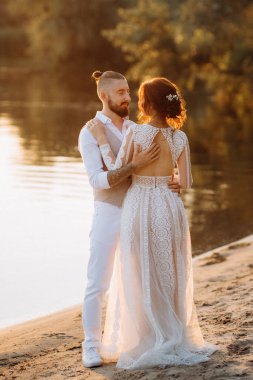 Gelin kız ve damat gün batımında nehrin kenarında