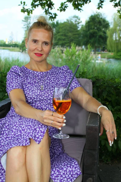 Bir plaj salonunda oturmuş, Aperol içen çekici bir kadının portresi.