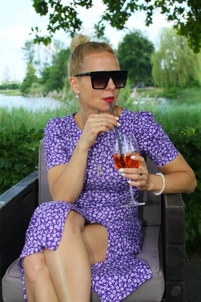 Bir plaj salonunda oturmuş, Aperol içen çekici bir kadının portresi.