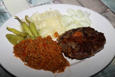 Biftek, djuvec pilavı, lahana salatası, pepperoni ve soğandan oluşan Balkan yemeği pljeskavica bir tabakta sunuldu,