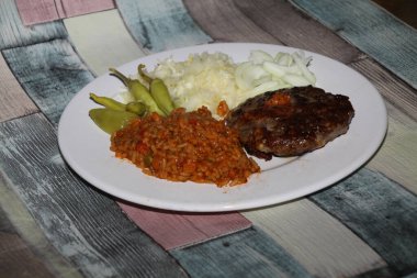 Biftek, djuvec pilavı, lahana salatası, pepperoni ve soğandan oluşan Balkan yemeği pljeskavica bir tabakta sunuldu,