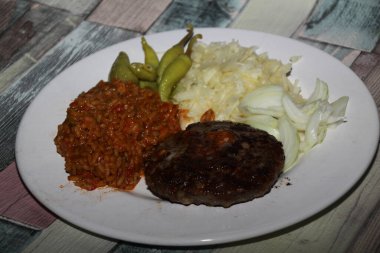 Biftek, djuvec pilavı, lahana salatası, pepperoni ve soğandan oluşan Balkan yemeği pljeskavica bir tabakta sunuldu,