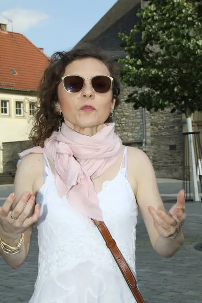 Beyaz elbiseli çekici bir kadın Paderborn 'daki katedral meydanında yoldan geçen biriyle iletişim kuruyor.