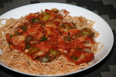 Makarnanın spagetti, balık, kapari, zeytin, domates, domates sosu ve bitkilerle yakın çekimi,
