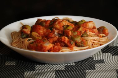 Makarnanın spagetti, balık, kapari, zeytin, domates, domates sosu ve bitkilerle yakın çekimi,