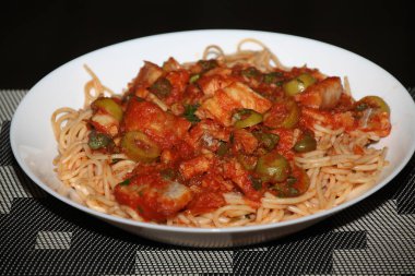 Makarnanın spagetti, balık, kapari, zeytin, domates, domates sosu ve bitkilerle yakın çekimi,