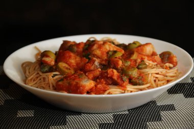 Makarnanın spagetti, balık, kapari, zeytin, domates, domates sosu ve bitkilerle yakın çekimi,