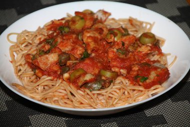 Makarnanın spagetti, balık, kapari, zeytin, domates, domates sosu ve bitkilerle yakın çekimi,
