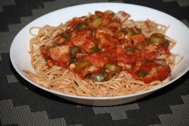Makarnanın spagetti, balık, kapari, zeytin, domates, domates sosu ve bitkilerle yakın çekimi,