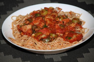 Makarnanın spagetti, balık, kapari, zeytin, domates, domates sosu ve bitkilerle yakın çekimi,