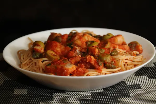 Makarnanın spagetti, balık, kapari, zeytin, domates, domates sosu ve bitkilerle yakın çekimi,