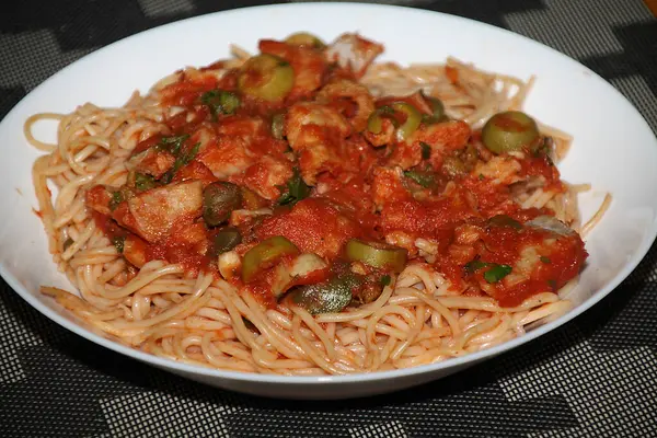 Makarnanın spagetti, balık, kapari, zeytin, domates, domates sosu ve bitkilerle yakın çekimi,