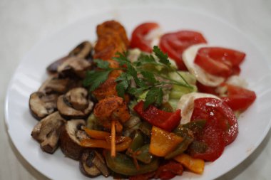 Beyaz bir tabakta servis edilen tavuk şişi, domates, mozzarella, biber, ton balığı, mantar ve marul...,