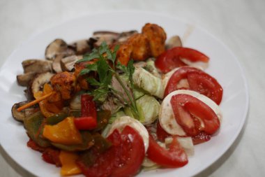 Beyaz bir tabakta servis edilen tavuk şişi, domates, mozzarella, biber, ton balığı, mantar ve marul...,