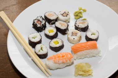 Farklı suşi türlerinin yakın çekimi, yemek çubuklarıyla beyaz bir tabakta servis edilir.,