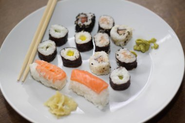 Farklı suşi türlerinin yakın çekimi, yemek çubuklarıyla beyaz bir tabakta servis edilir.,